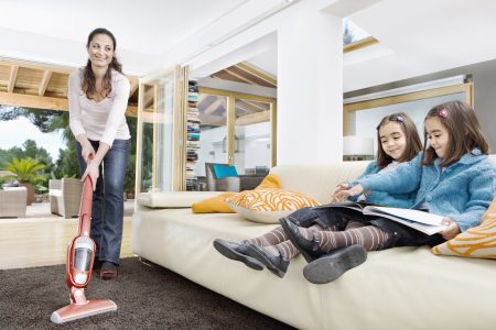 母亲用树棒吸尘清洗起居室地毯 孩子们边看沙发